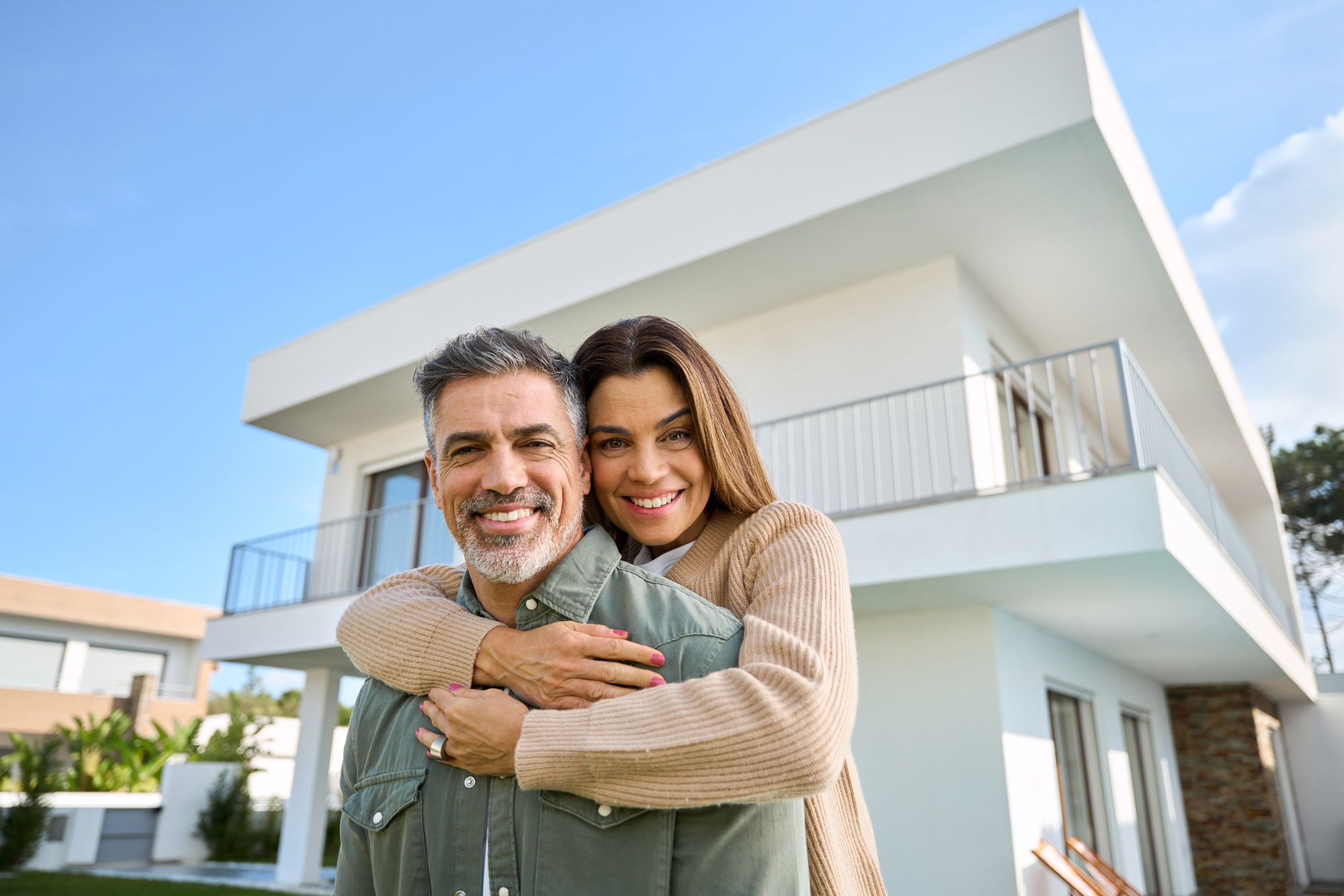 Happy smiling mature older family couple new home owners standing outside house.